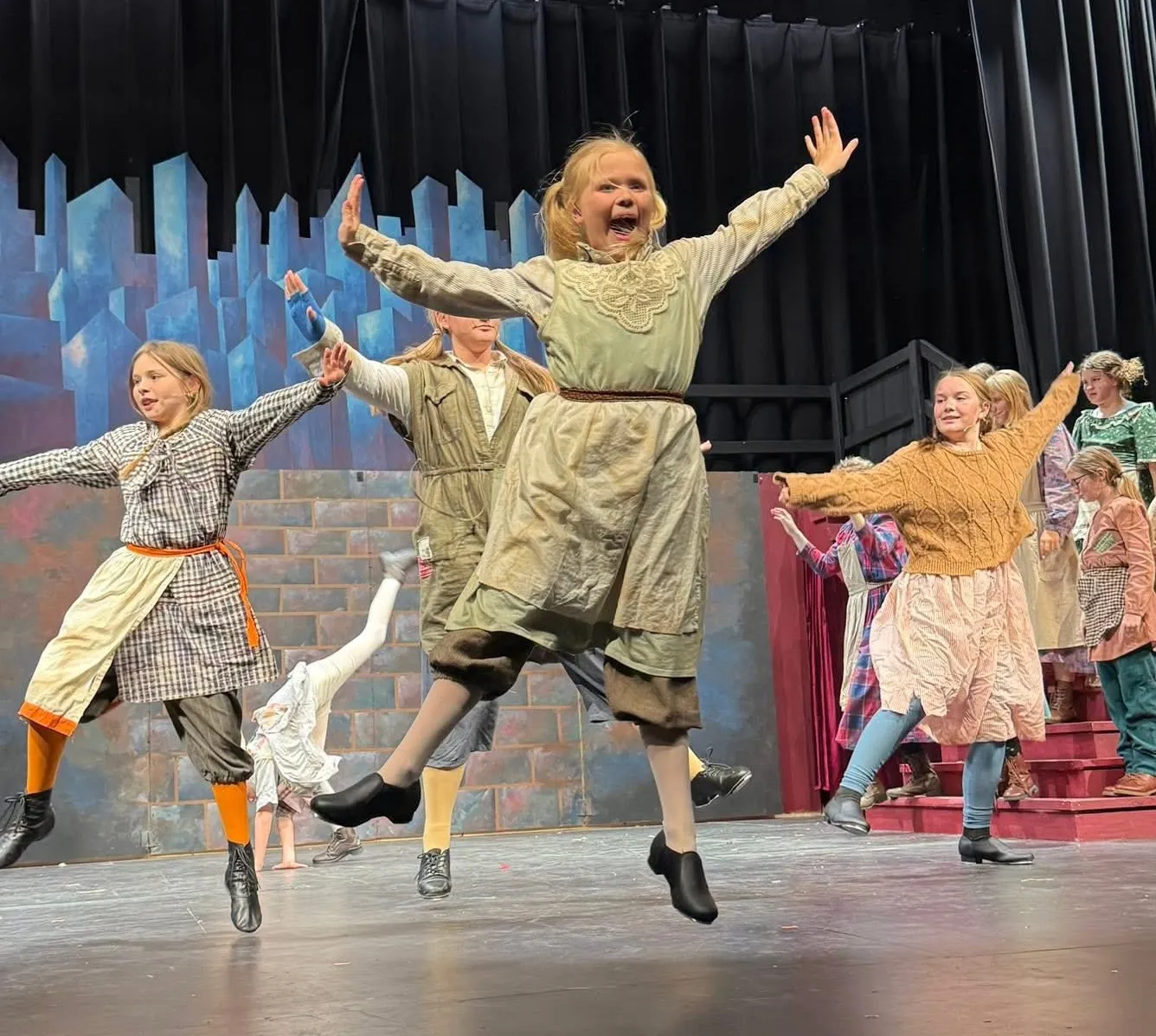 Children in costume joyfully dancing and jumping on stage during a theater performance.