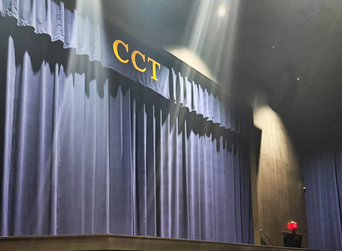 A stage with closed blue curtains and gold letters "CCT" above, spotlights shining down.