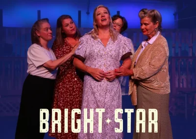 Five women in vintage costumes stand together on stage under blue lighting, with "Bright Star" text displayed.