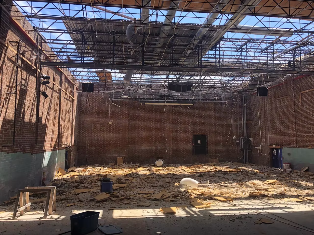 A large room with a partially destroyed ceiling, exposed beams, and debris scattered across the floor.