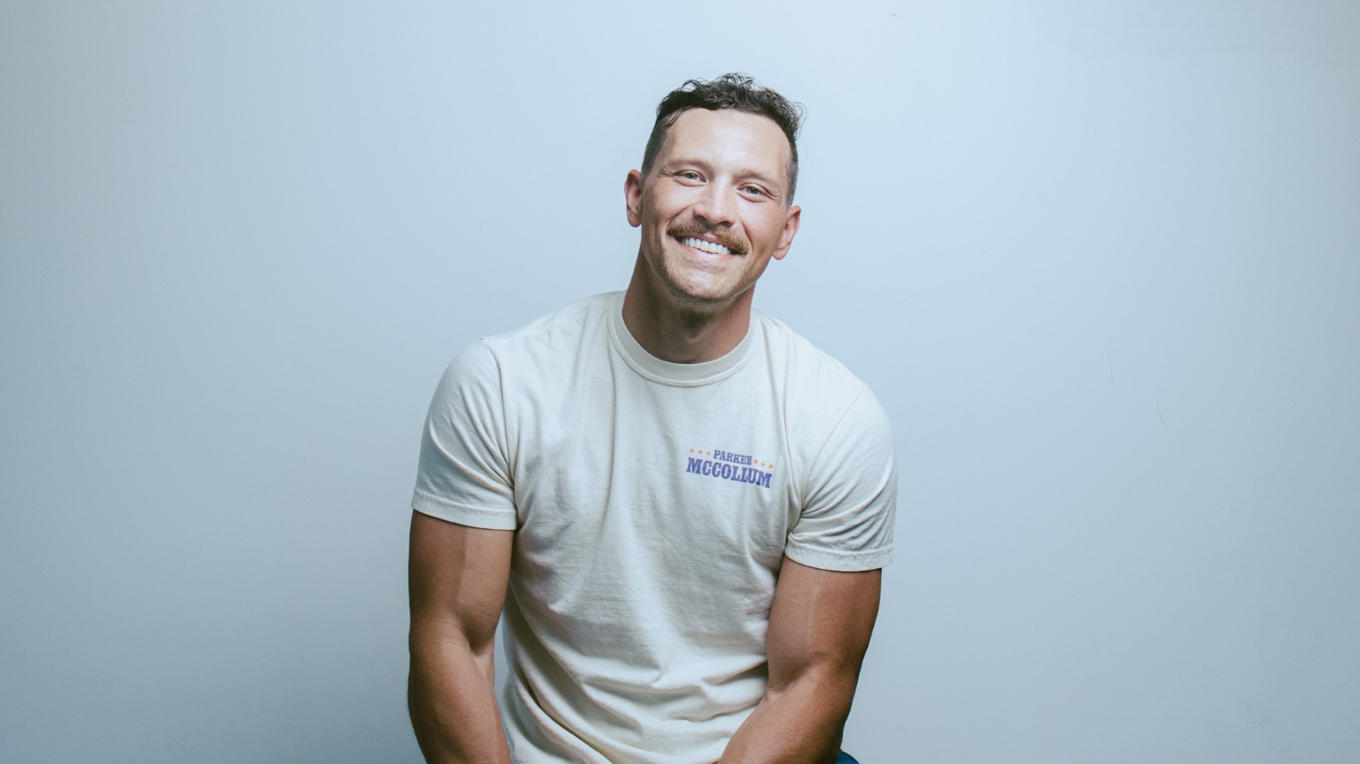 Smiling man in a white t-shirt sits against a plain light background.